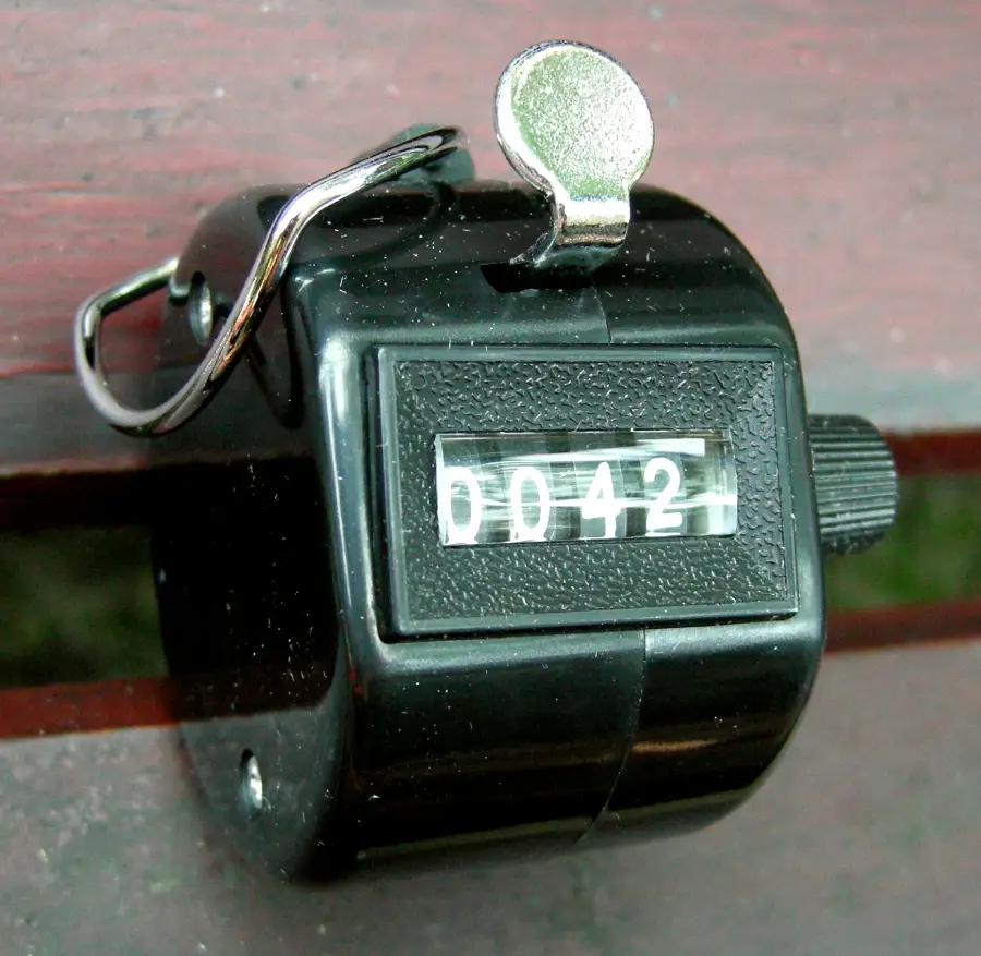 A black handheld tally counter displays the number 0042. It is resting on a wooden surface.