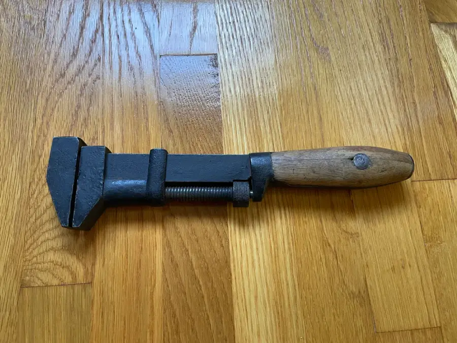 An old adjustable wrench with a wooden handle and metal head is lying on a polished wooden floor.