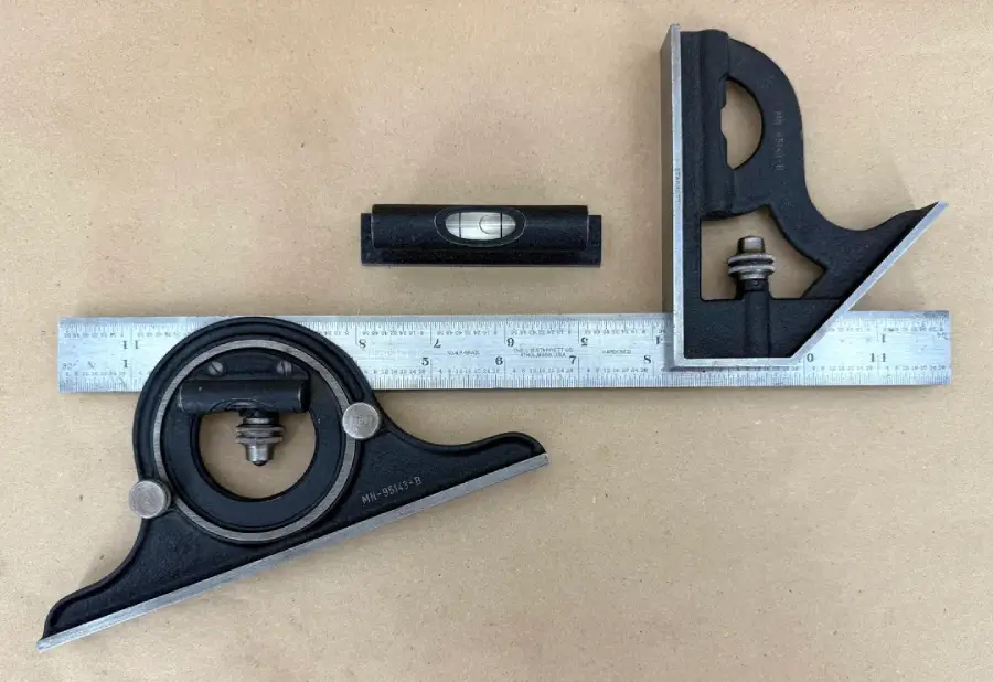 A metal ruler with a combination square, a speed square, and a small bubble level placed on a brown surface. All tools are arranged neatly.