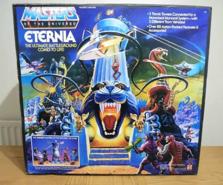 Box for “Masters of the Universe: Eternia” playset featuring a blue tiger-lion fortress, monorail, toy figures, and action scenes, with colorful cosmic and battle artwork in the background.