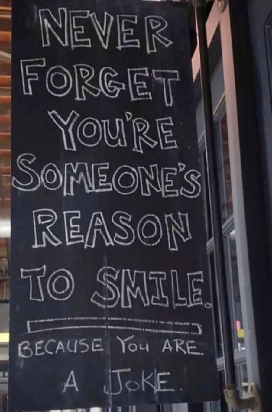 A chalkboard sign reads: “Never forget you’re someone’s reason to smile. Because you are a joke.” The text is written in uppercase and lowercase chalk letters.