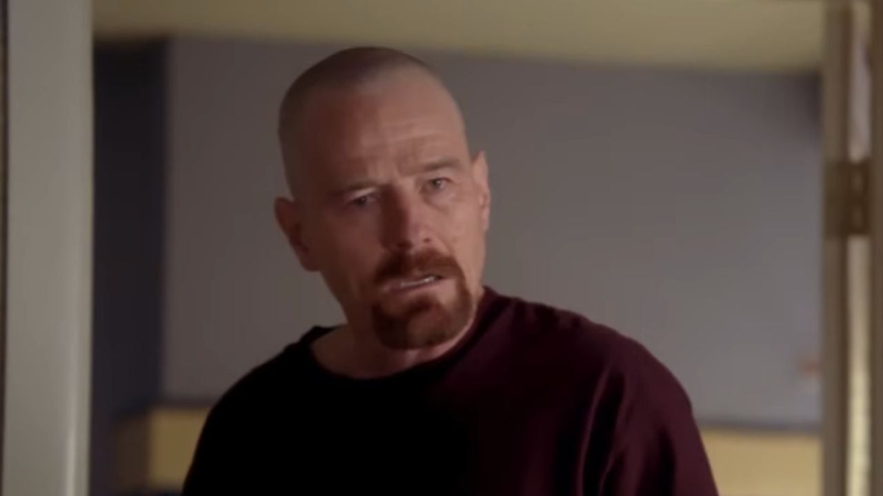 A bald man with a goatee wearing a dark shirt stands indoors, looking intensely forward with a serious expression.