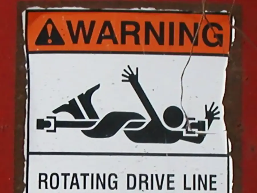 Warning sign showing a stick figure being caught in a rotating drive line, indicating a risk of entanglement and injury. Bold “WARNING” text is above the illustration, with smaller text: “ROTATING DRIVE LINE.”