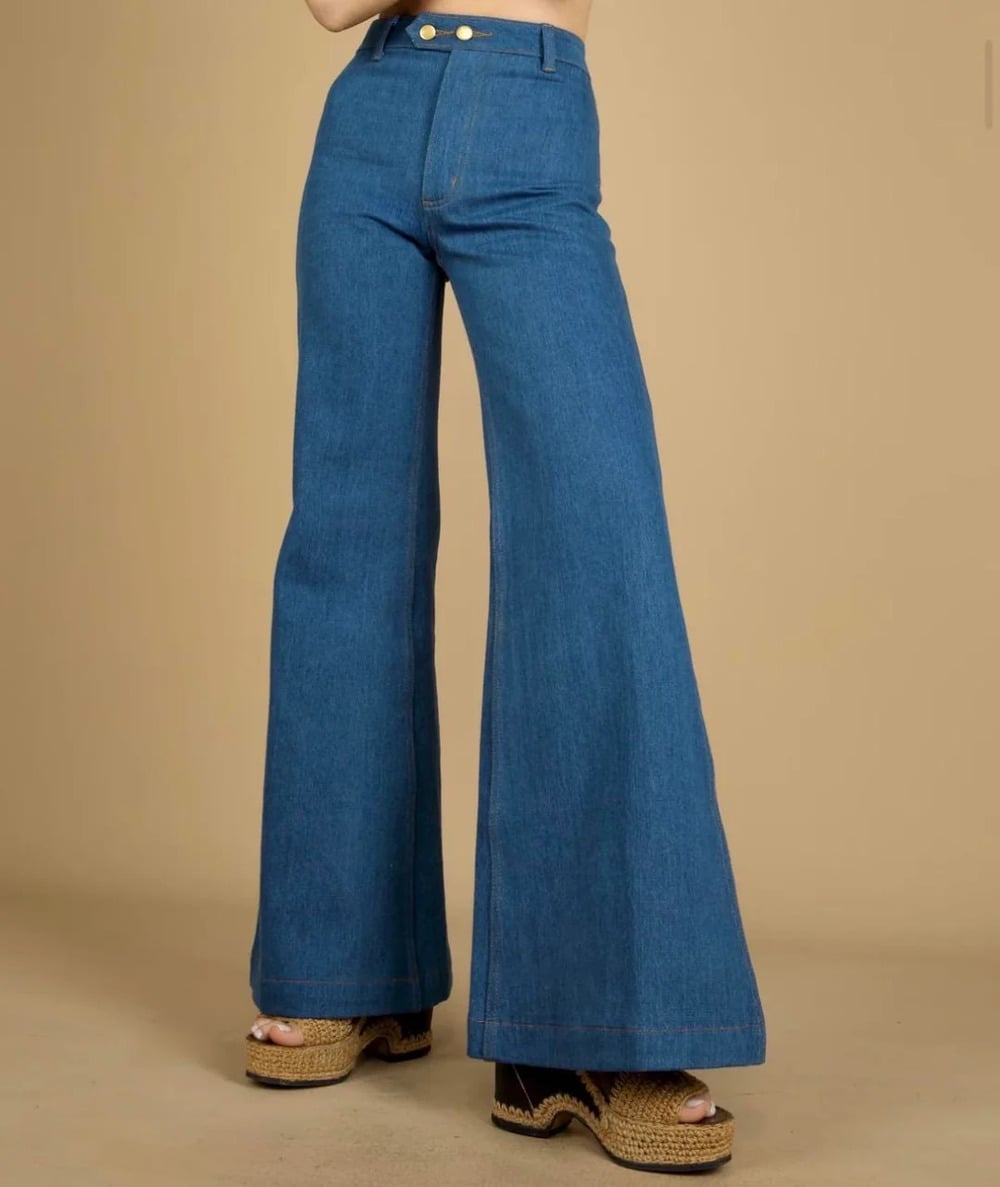 Person wearing high-waisted, wide-leg blue jeans and platform woven sandals, standing against a plain beige background. The person’s upper body is not visible.
