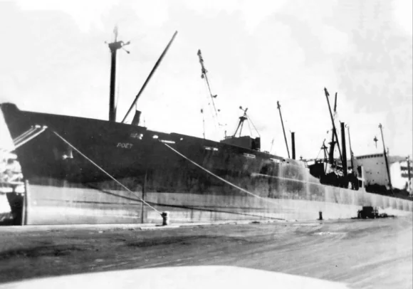 Black and white photo of a large cargo ship named “Poet” docked at a port, with cranes on deck and industrial structures in the background.