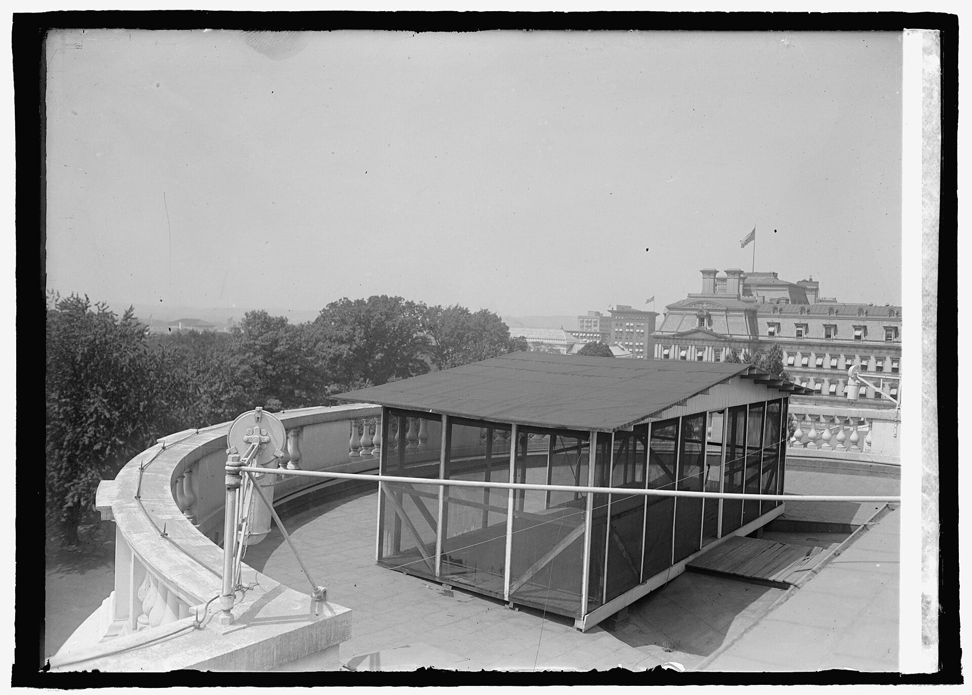 A screened-in, flat-roofed structure sits on a curved stone terrace overlooking a city skyline.