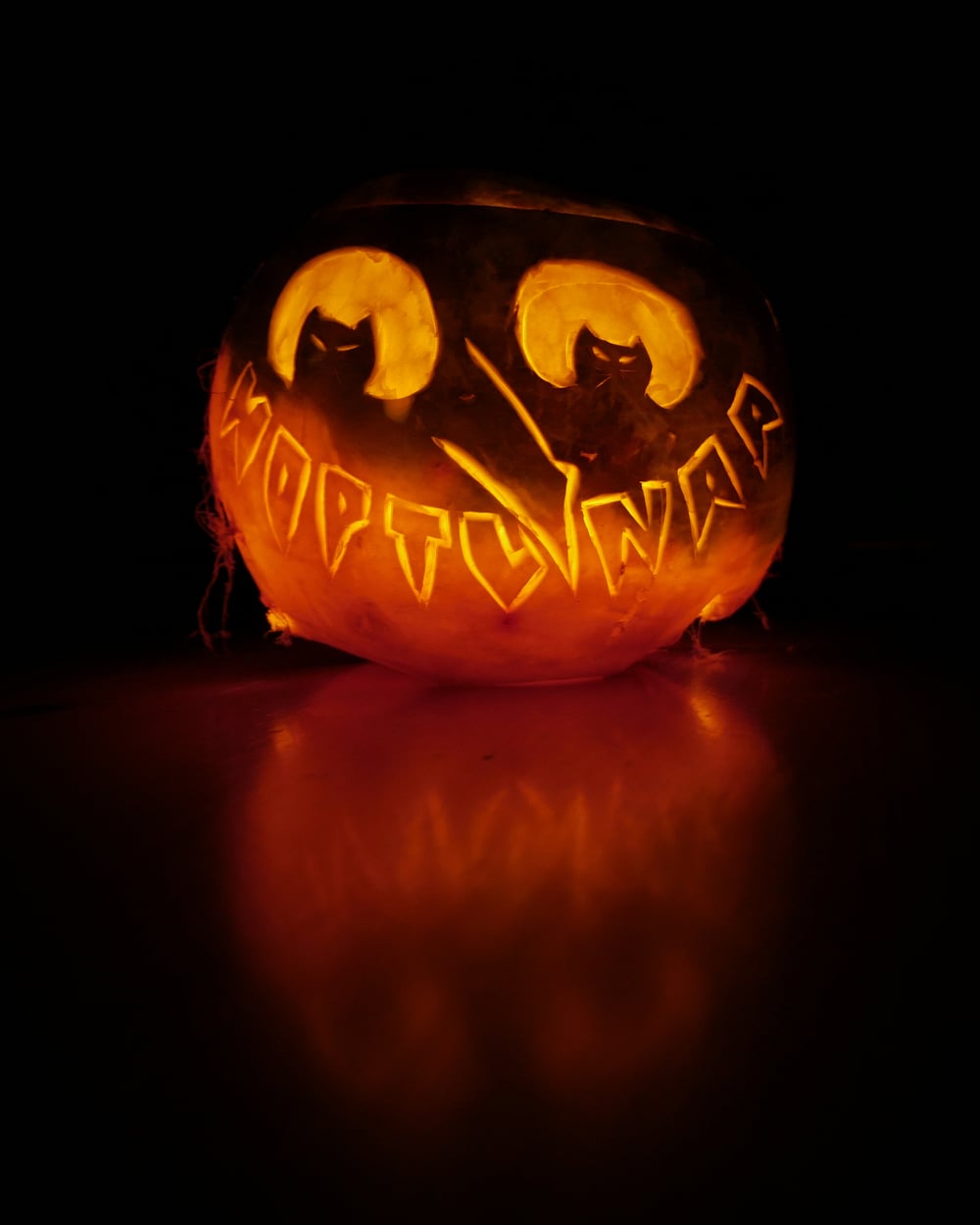 A glowing jack-o’-lantern carved with the text “WOPTLUNAR” and two cat-like shapes above the letters.