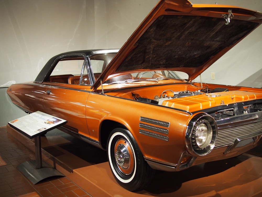 A copper-colored 1963 Chrysler Turbine car with its hood open, displayed in a museum with an informational placard nearby.
