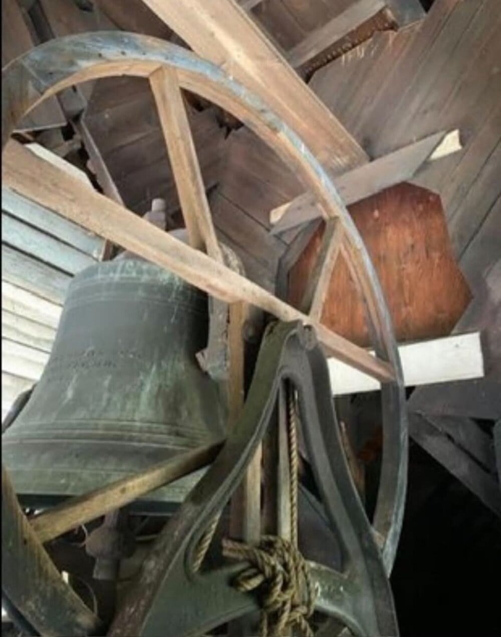 A large metal bell mounted on a wooden frame inside a bell tower.