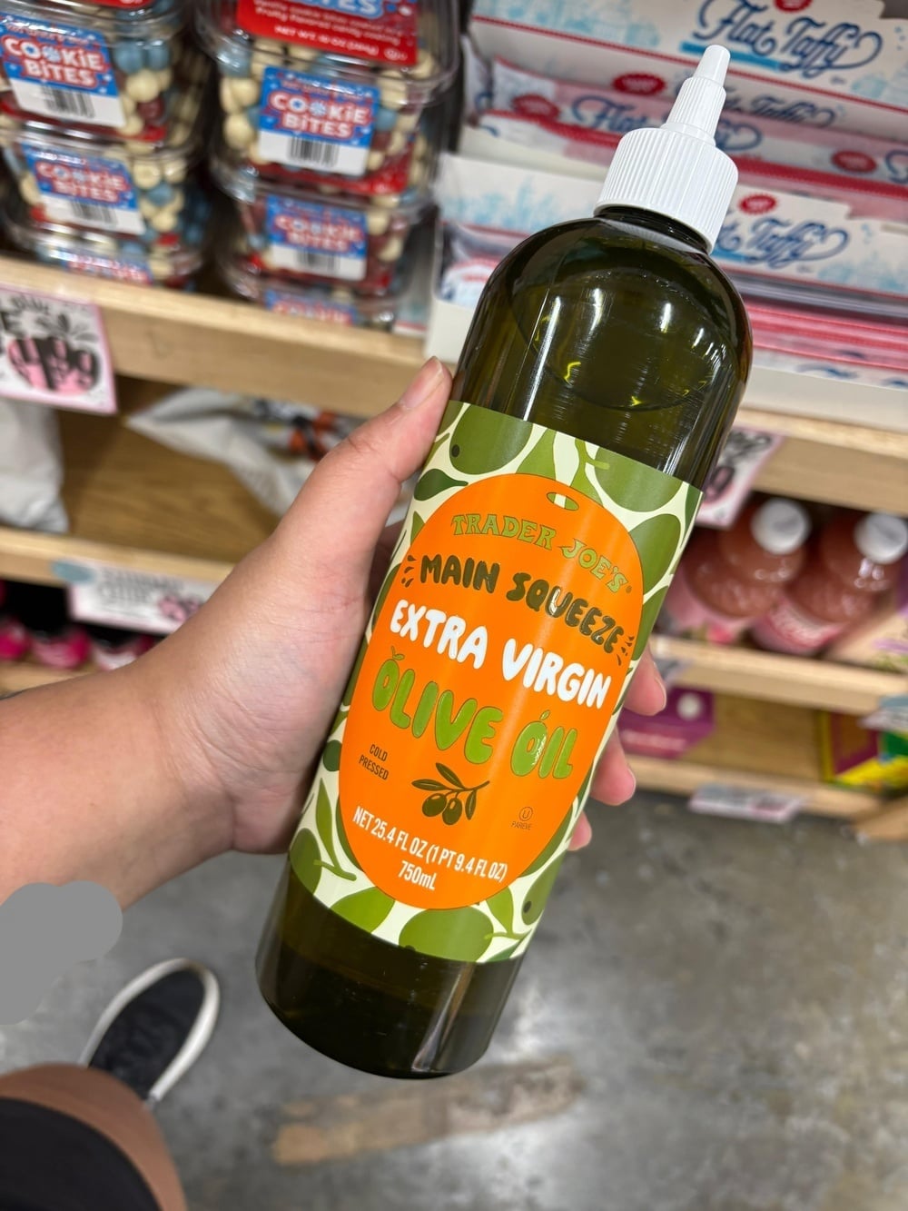 A hand holds a bottle of Trader Joe’s Main Squeeze Extra Virgin Olive Oil with a green olive-patterned label.