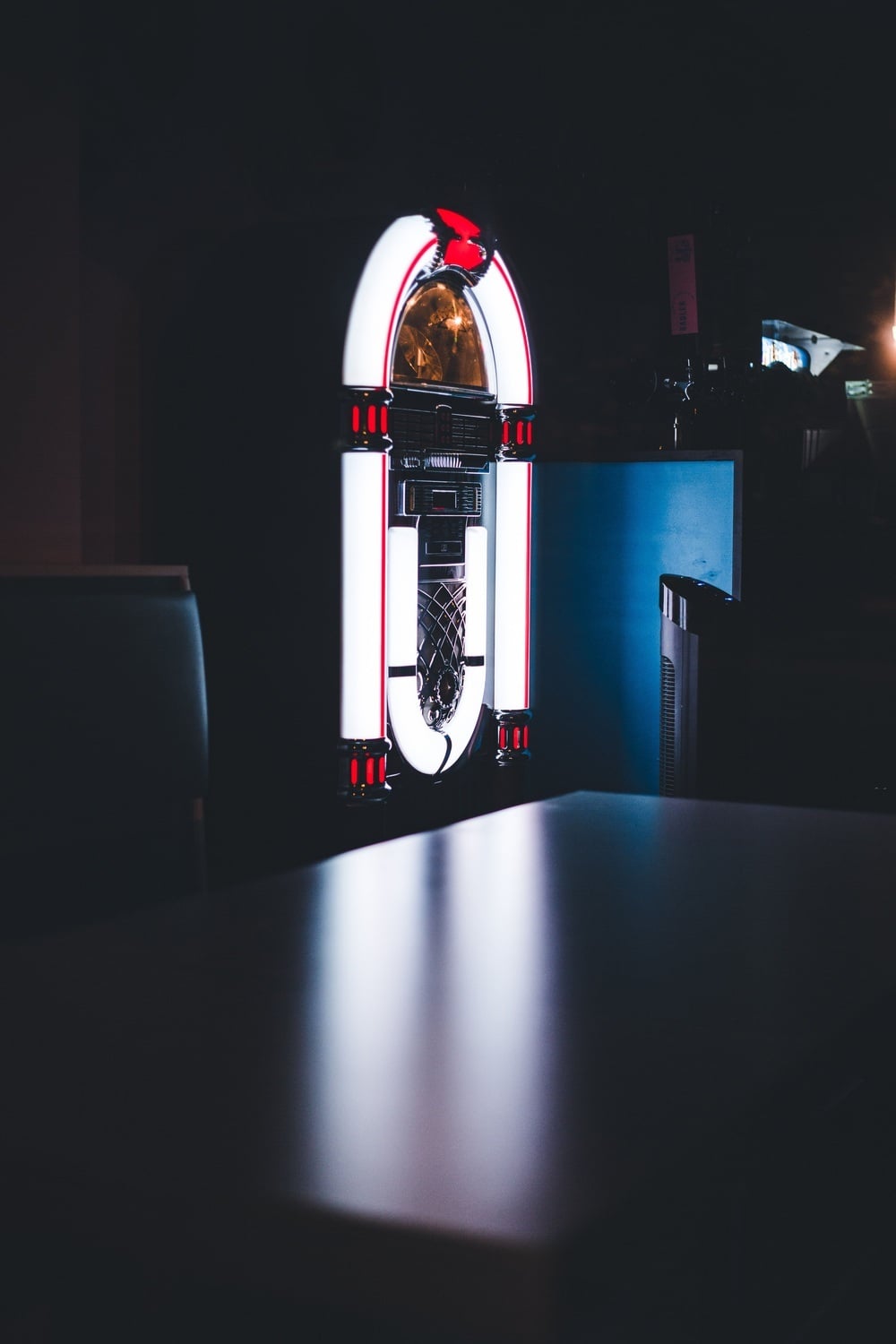 A glowing, retro-style jukebox standing in a dimly lit room behind a table.