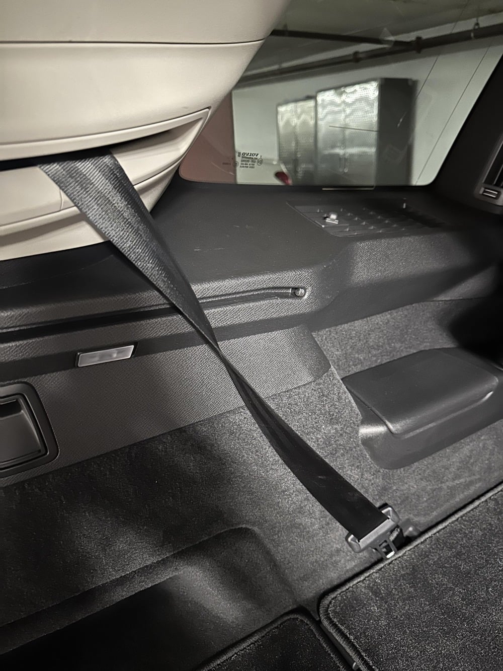 A black seatbelt strap hanging from the interior side panel of a car trunk.