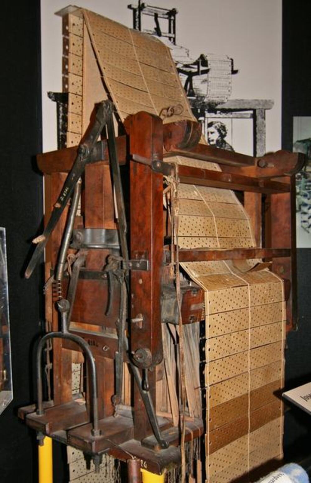 A vintage wooden Jacquard loom with a long strip of perforated pattern cards feeding through the mechanism.