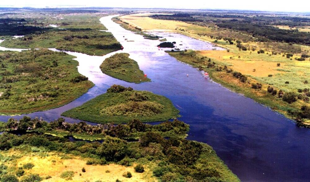 Aerial view of a river winding through wetlands and grasslands with small, vegetated islands in the water.