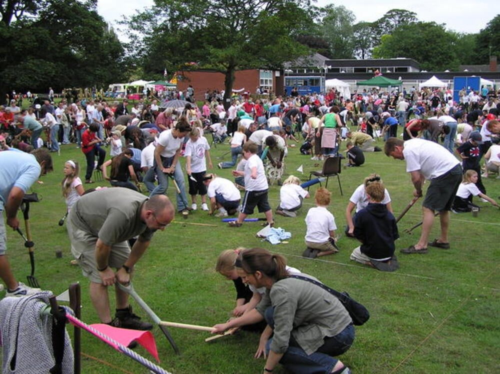 People bend over small plots of grass during an outdoor event.