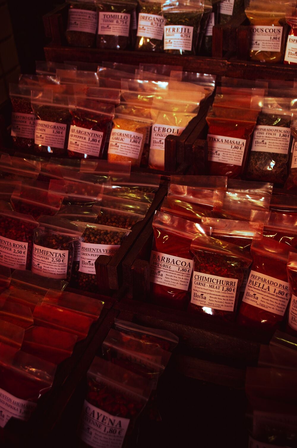 Rows of various spices in clear plastic bags, each labeled with the name of the spice and its price.