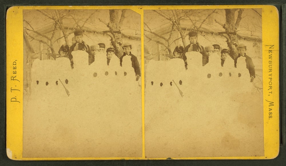 A stereoscopic photograph of a group of children standing behind a line of snowmen in front of a house, titled P.T. Reed, Newburyport, Mass.