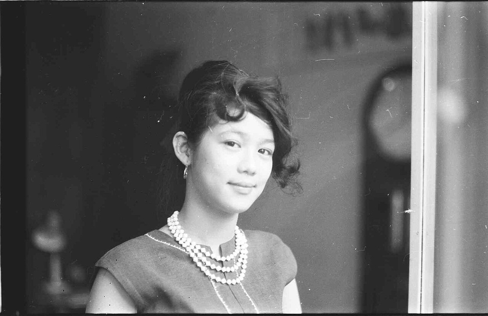 A young woman with a side-swept hairstyle wearing a multi-strand pearl necklace.