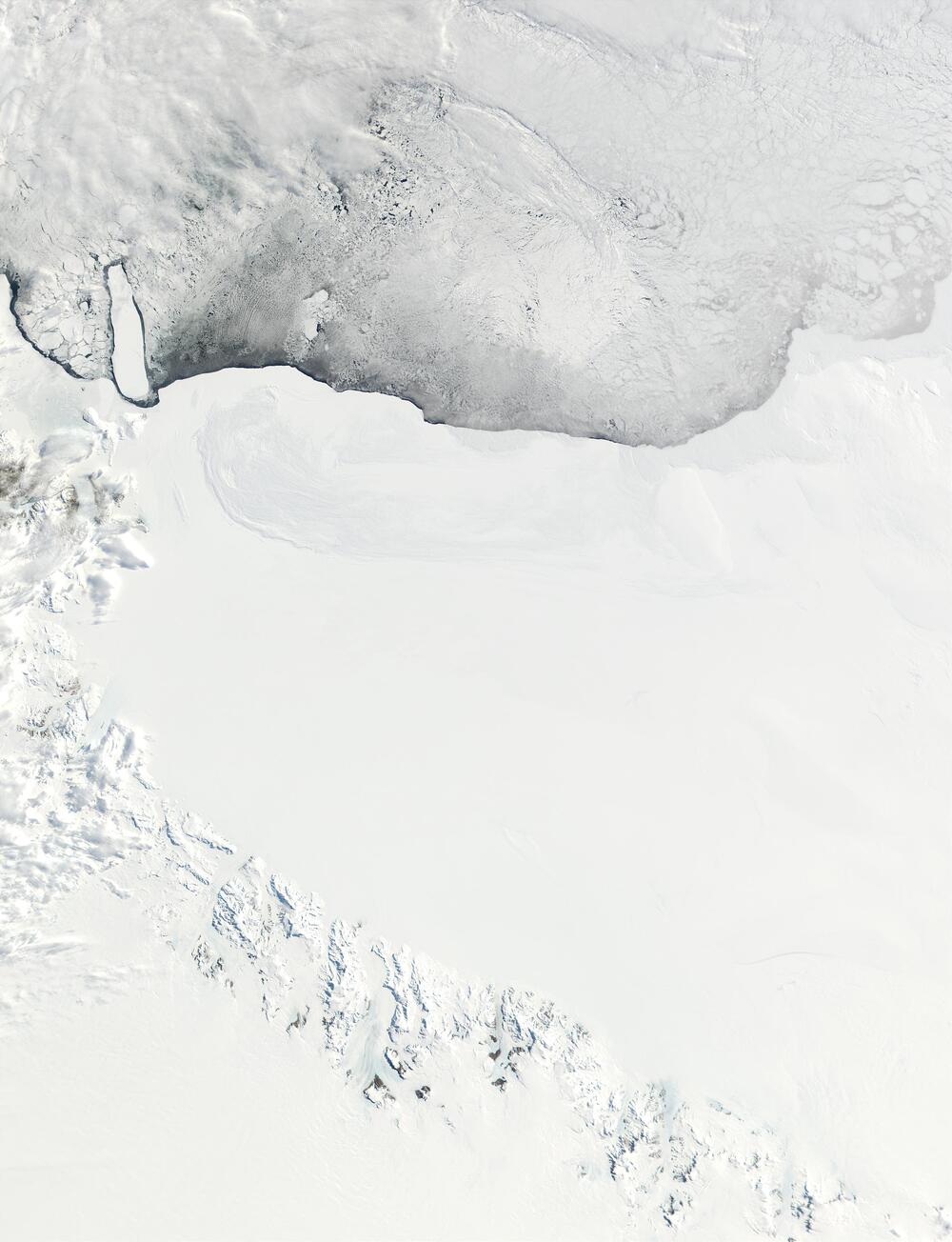 Satellite view of a vast, white ice field bordering a dark, partially frozen body of water.