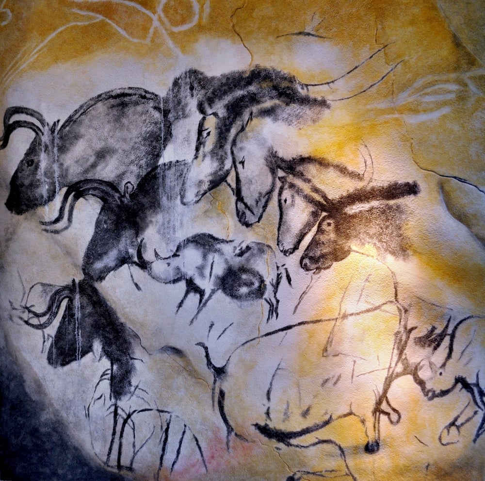 Cave painting of several bison and other animals in charcoal on a textured rock wall.