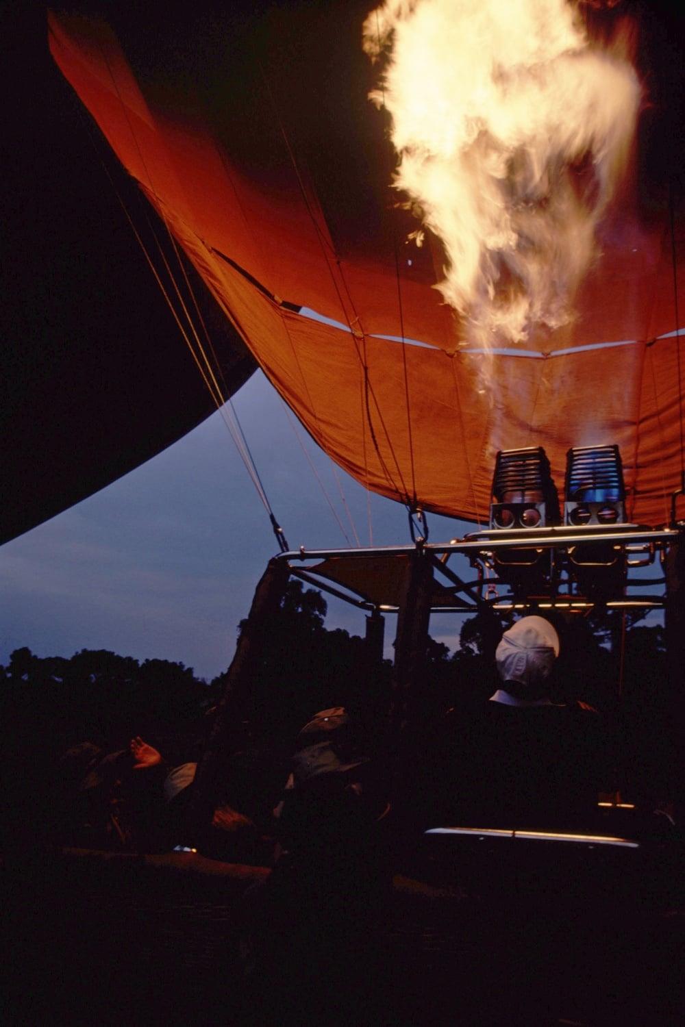 A person in a hot air balloon basket looking up at the burner flame igniting the envelope above.