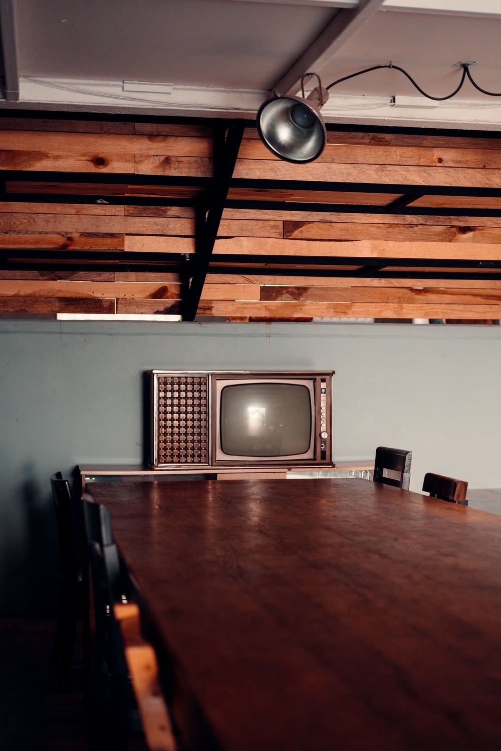 A vintage television set sits on a cabinet behind a large wooden dining table.