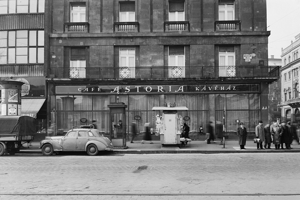Street-level view of the Cafe Astoria building with pedestrians and a vintage car parked out front.