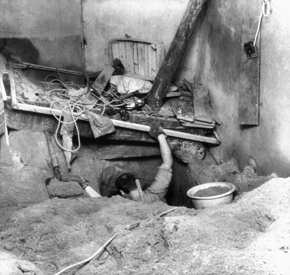 A person reaches out of a tunnel entrance beneath a cluttered floor.