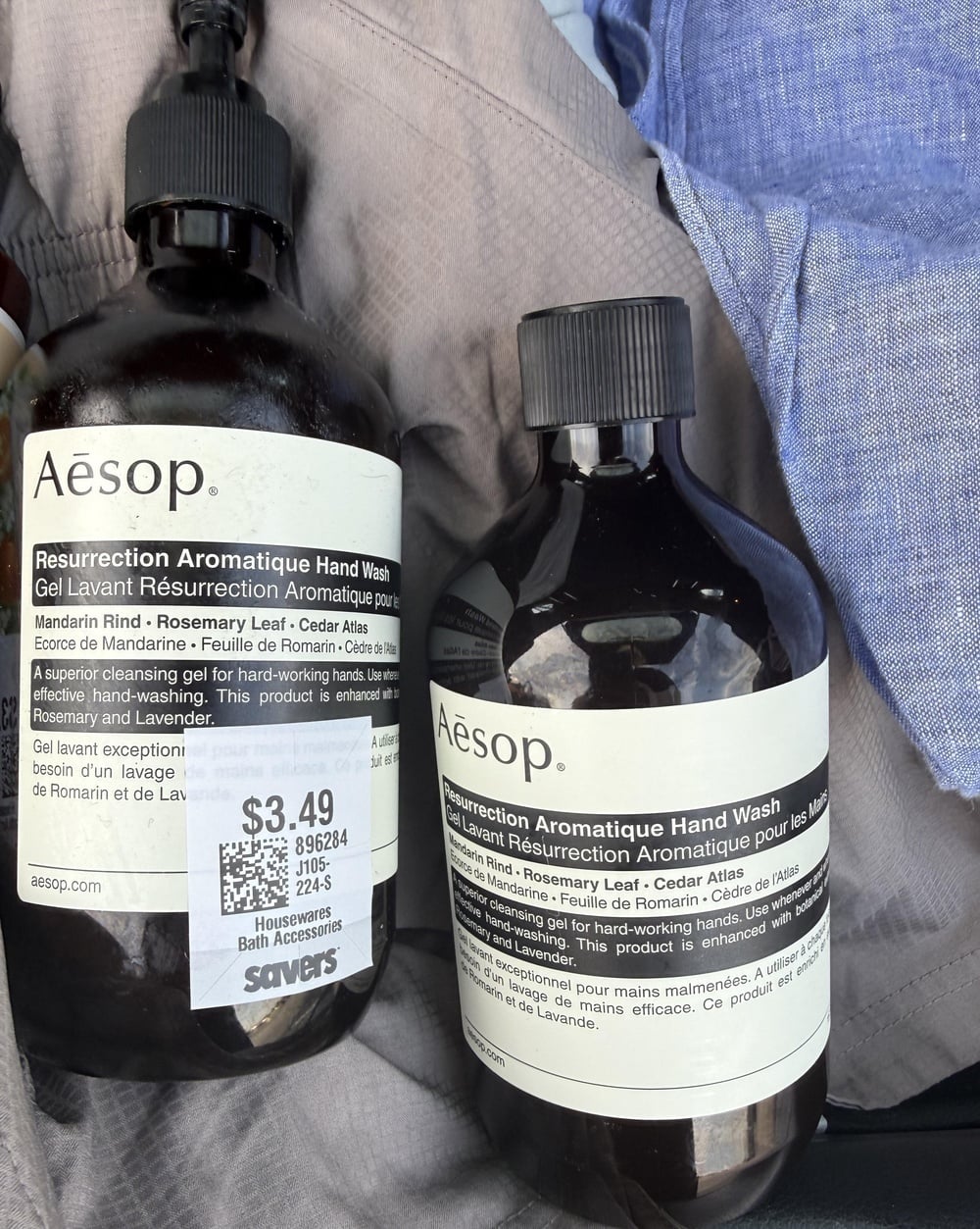Two amber bottles of Aesop Resurrection Aromatique hand wash sitting on blue fabric, with a Savers price tag of $3.49 on the left bottle.