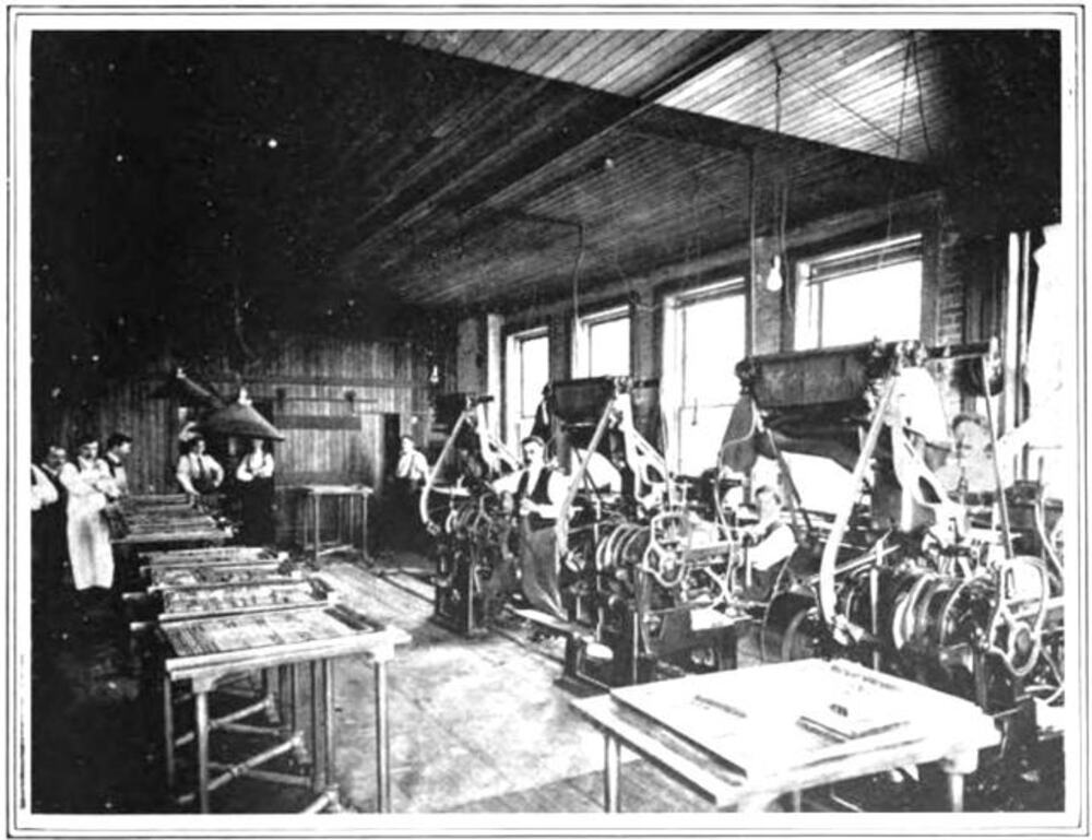 Black and white photo of men working at printing presses in a workshop.