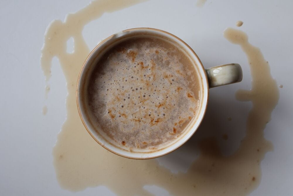 A cup of coffee surrounded by spills on a white surface.