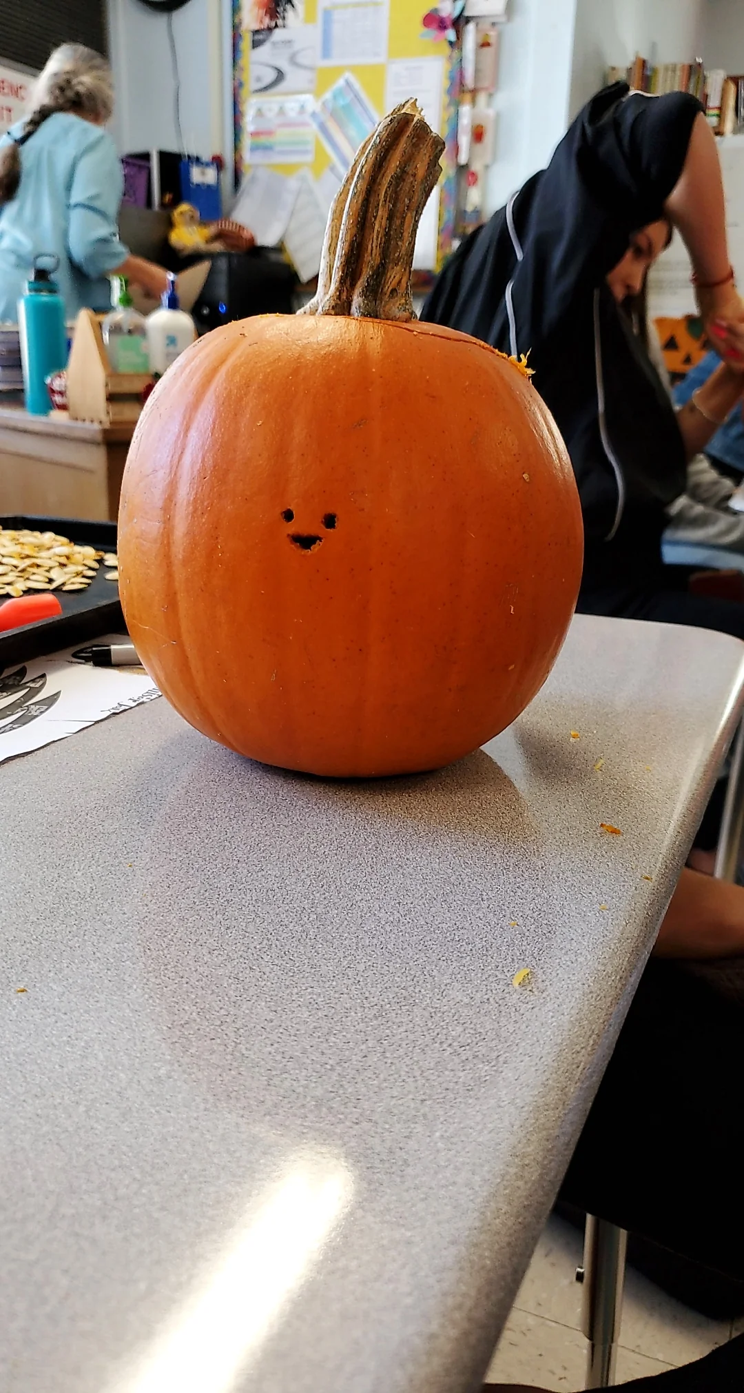 A small, carved pumpkin with a tiny, simple smiley face sits on a classroom desk.