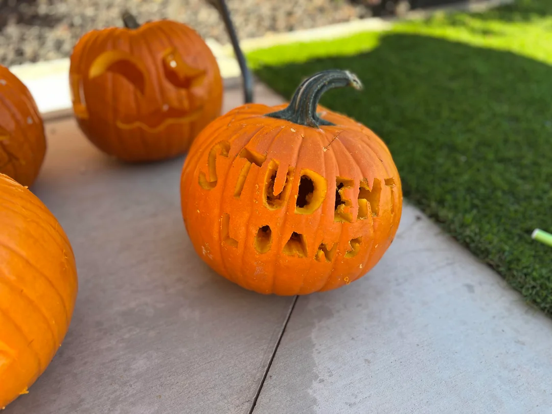 A carved pumpkin with the words “STUDENT LOANS” cut into its front, sitting on a concrete surface near other pumpkins.