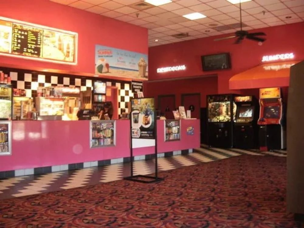 A brightly lit snack bar and arcade area with pink walls, a black-and-white checkered backsplash, and a patterned carpet.