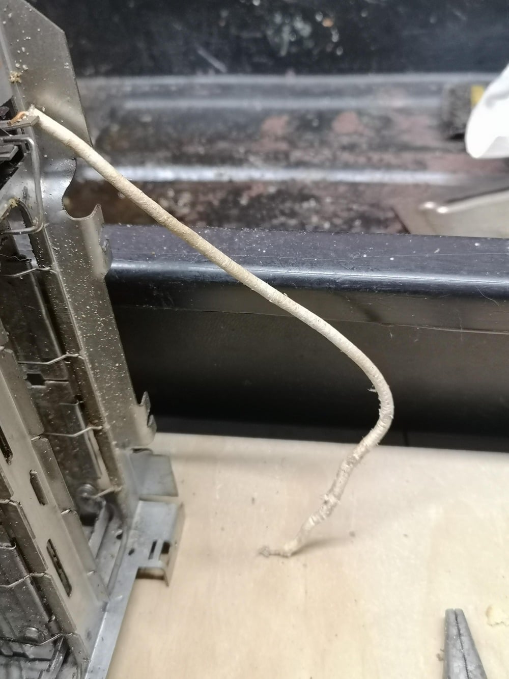 A dusty, tangled wire extends from a metal electronic component, resting on a beige surface. The background is dark and partially blurred.