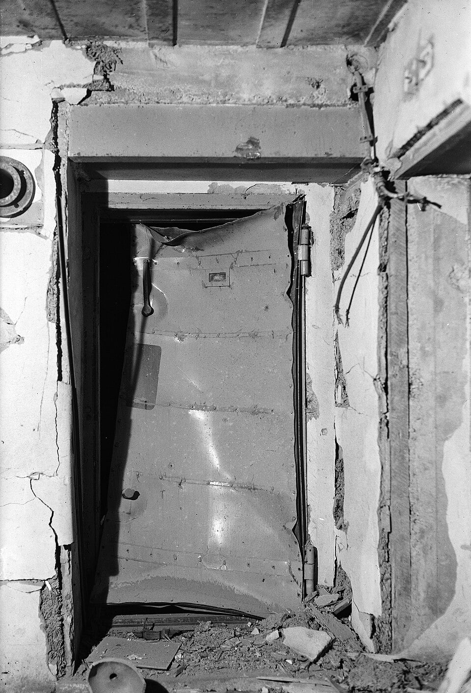 A heavily damaged metal door hangs askew in a crumbling concrete doorway.