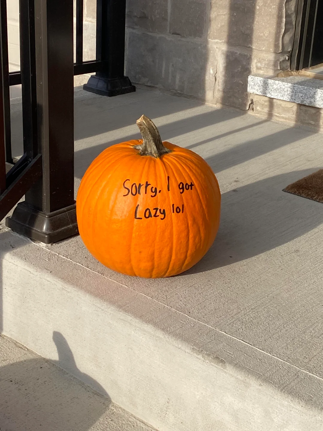 An orange pumpkin sitting on a porch with the words “Sorry. I got lazy lol” written on it in black marker.