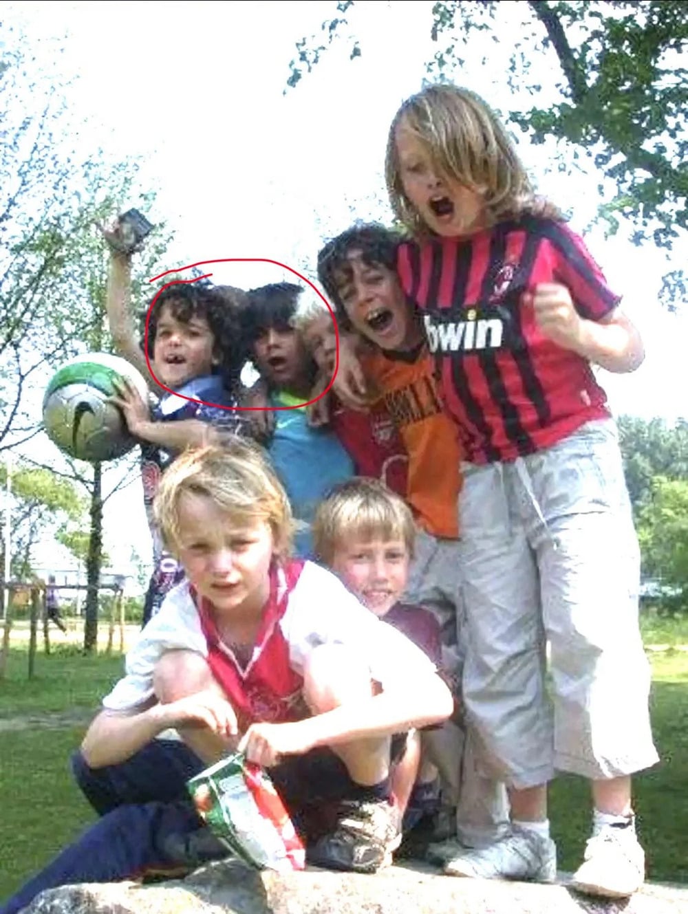 A group of six children posing together outdoors, with two of the children in the back row circled in red.