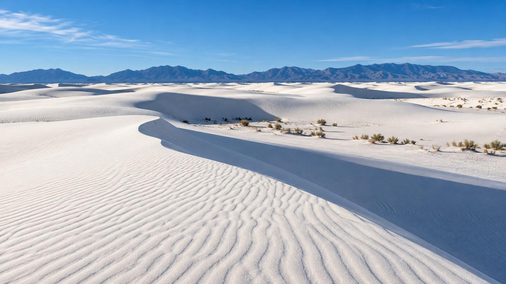 White gypsum sand dunes under a clear blue sky, with mountains in the distance.