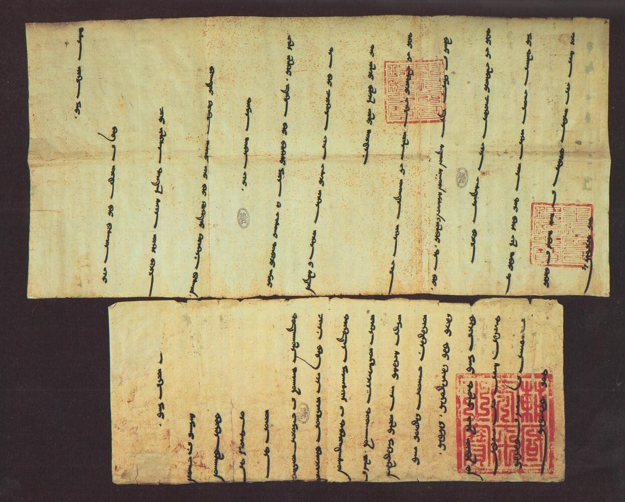 Two strips of ancient paper featuring vertical columns of handwritten Mongolian script and several red square ink stamps.
