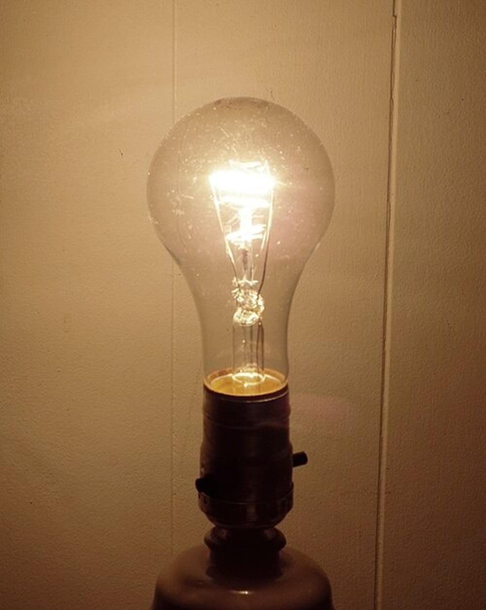 A lit incandescent light bulb screwed into a lamp socket.