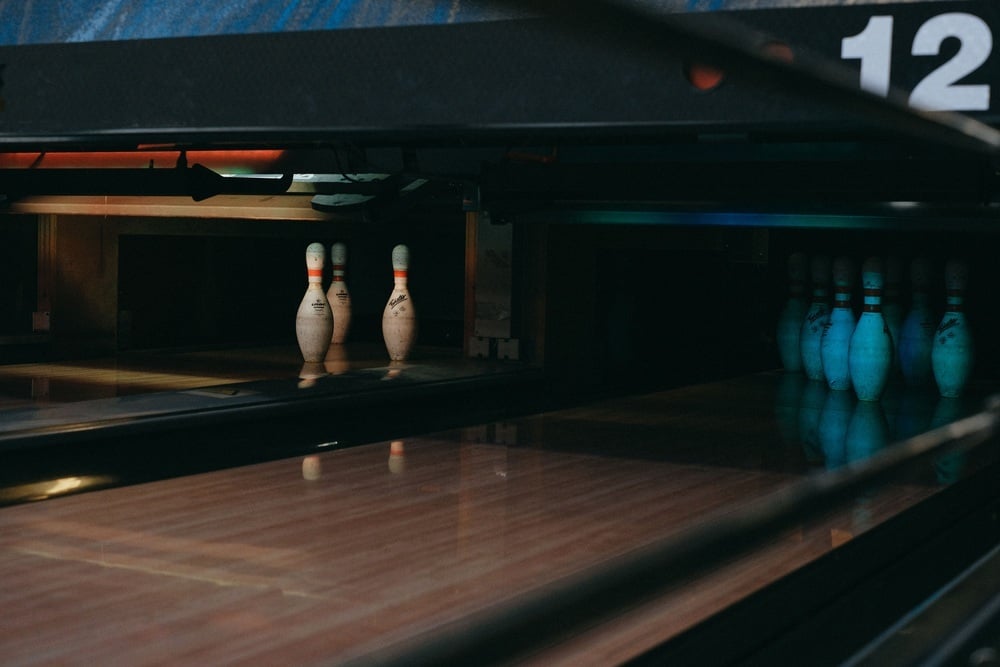 Three bowling pins standing on a lane in the distance, with a full set of ten pins positioned in the foreground.