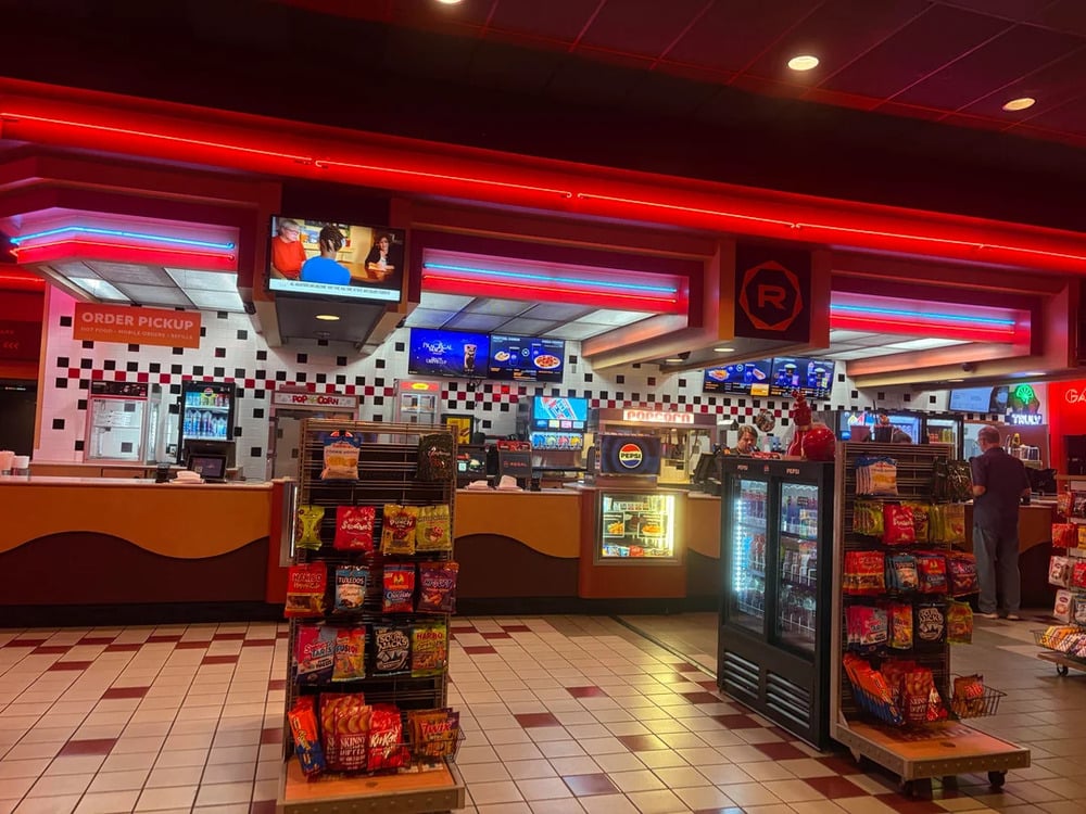 Concession stand at a movie theater with snack displays in the foreground and an order pickup counter in the back.