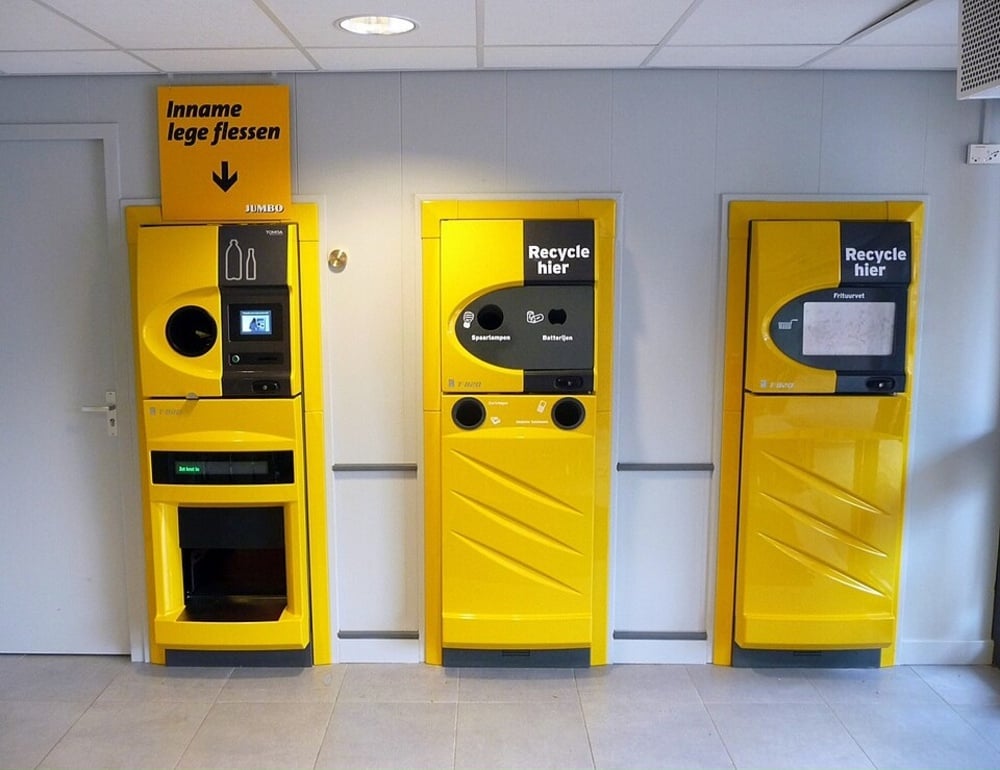 Three yellow recycling kiosks for bottles, light bulbs, batteries, and frying fat at a Jumbo store.
