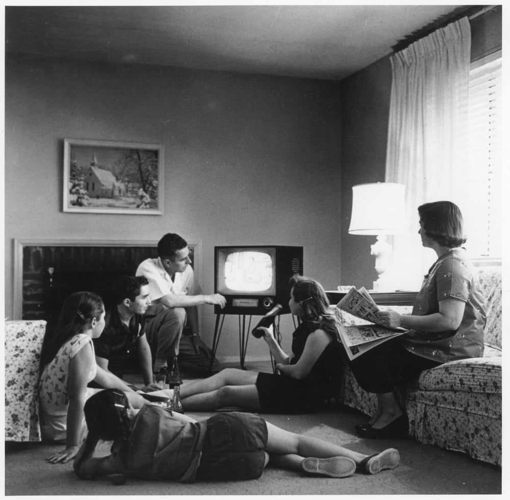 A family sits in a living room watching a television set.