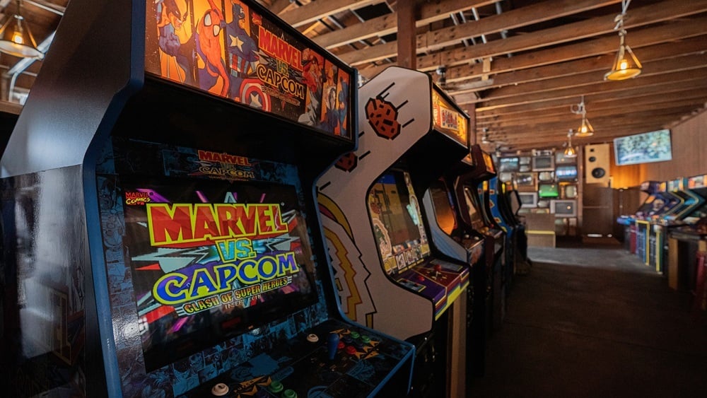 A row of vintage arcade game cabinets in an arcade, with a Marvel vs. Capcom machine in the foreground.