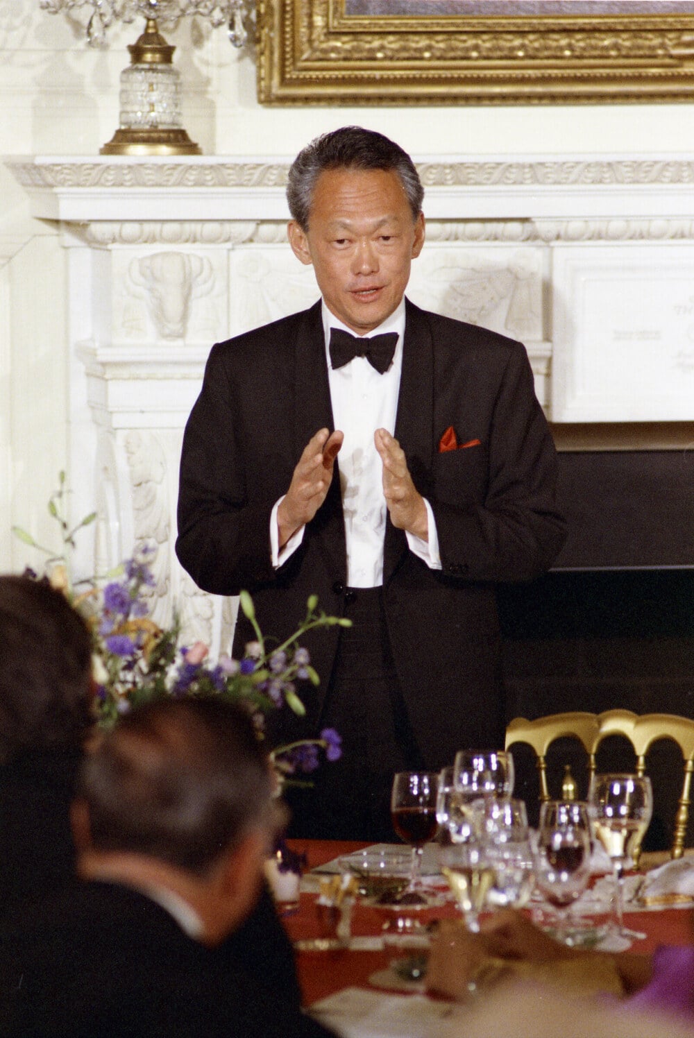 Lee Kuan Yew in a tuxedo stands and speaks at a dinner event.