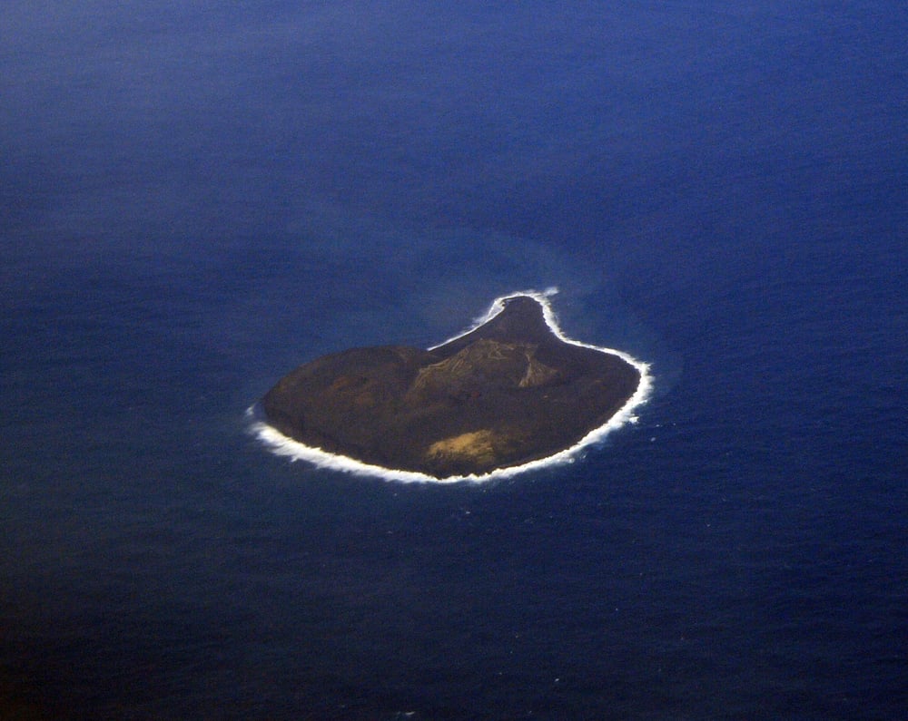 An aerial view of a heart-shaped volcanic island surrounded by dark blue ocean water.