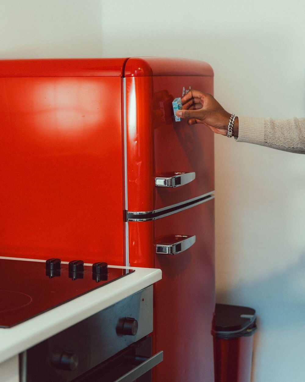 A hand reaches to place a blue magnet onto a bright red retro-style refrigerator.