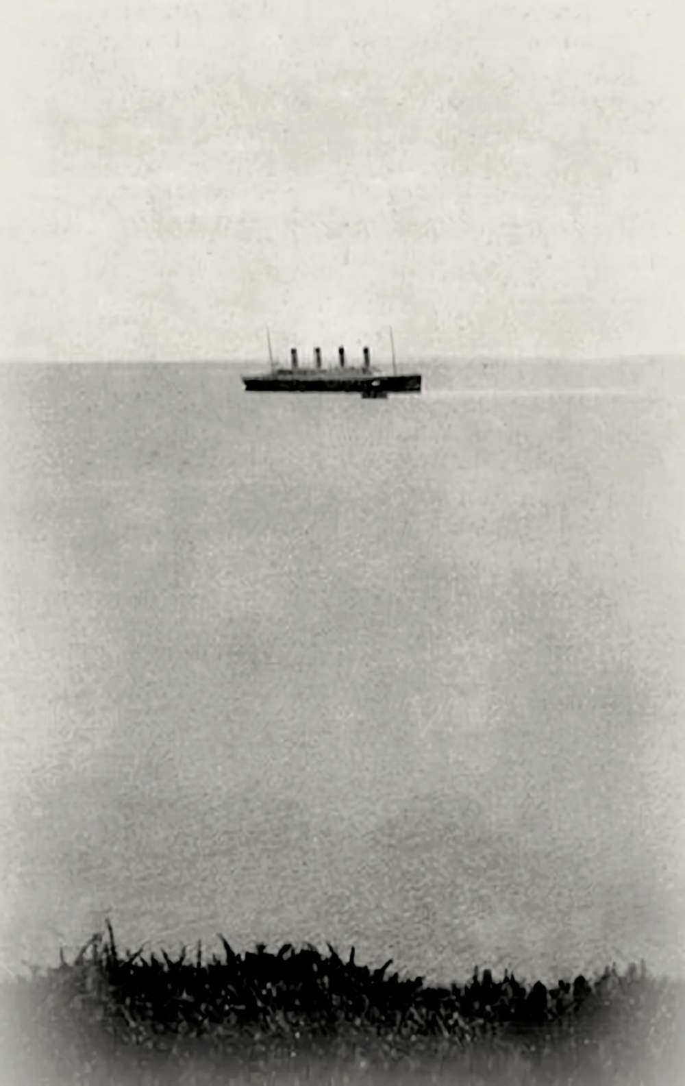 A large steamship with four smokestacks on a calm sea, viewed from a distance.